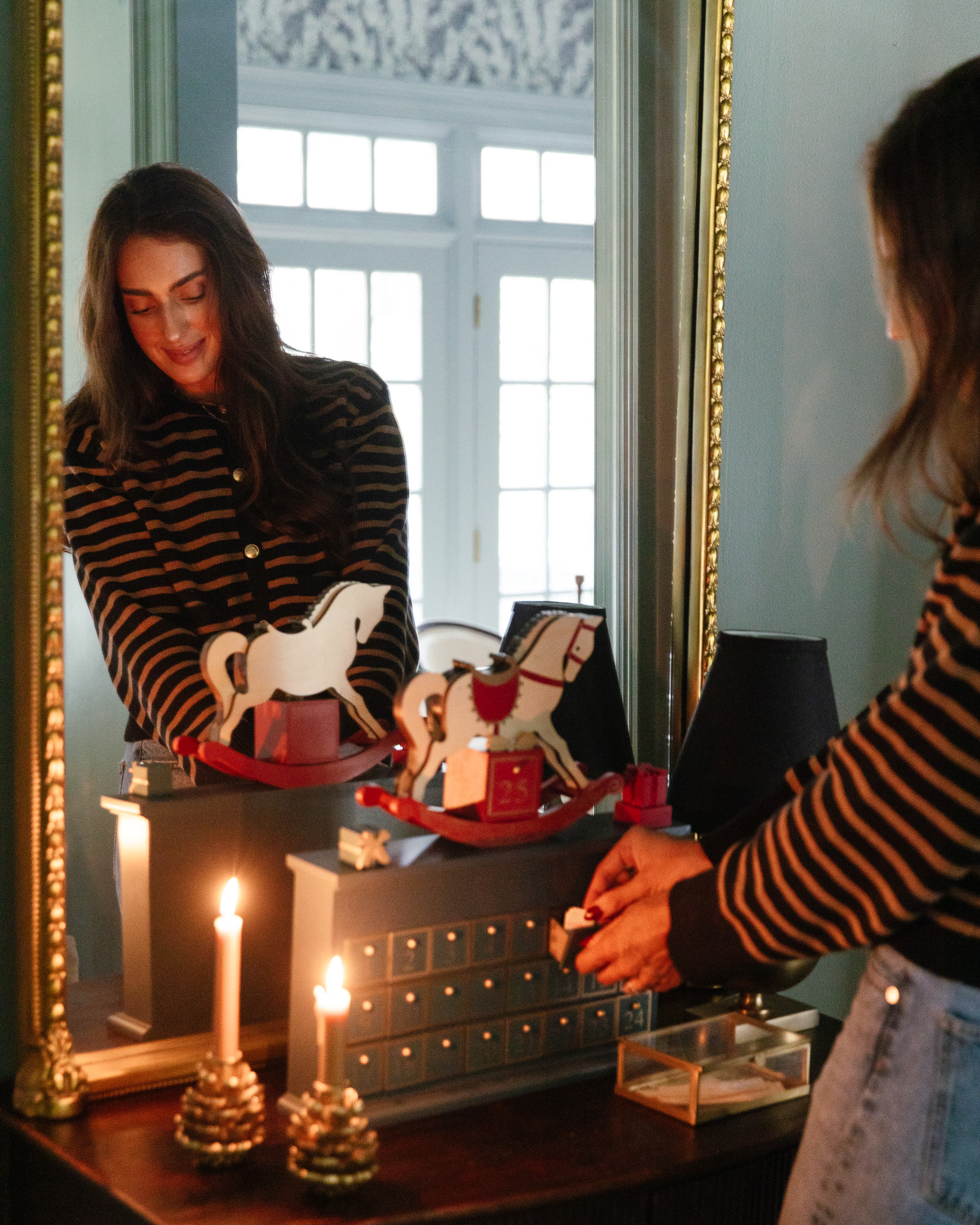 Julia opening the drawer of a dark green wood advent calendar with a vintage-looking rocking horse on top