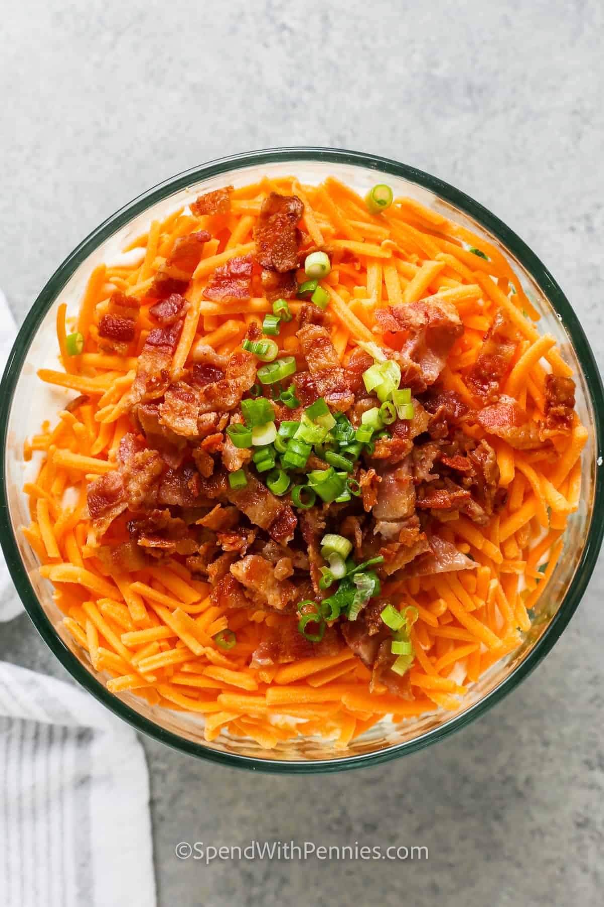 adding bacon and green onions to the top of a 7 Layer Salad