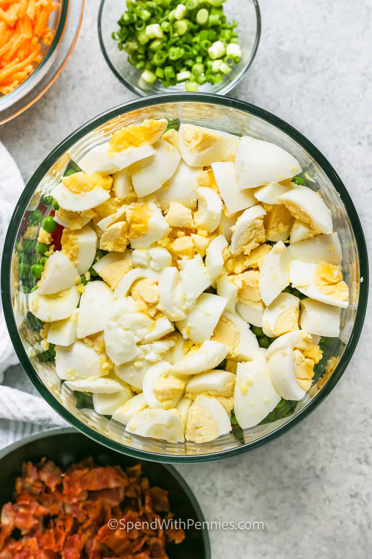 adding eggs to bowl to make 7 Layer Salad