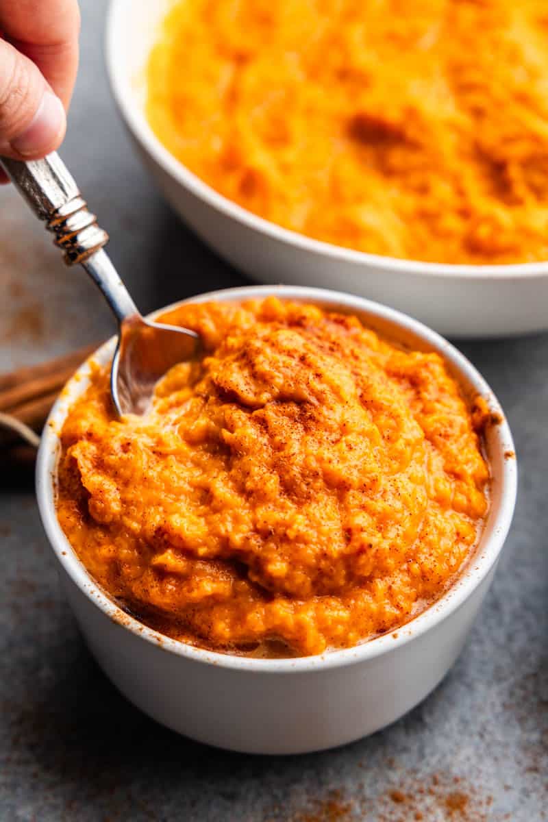 hand holding spoon in bowl of mashed sweet potatoes