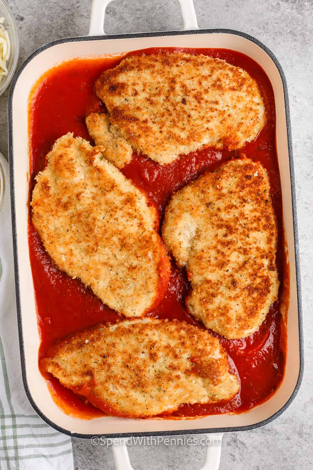This easy chicken parmesan recipe delivers a colorful and delicious main dish. Chicken breasts are breaded in crispy panko crumbs and then lightly pan-fried. Then the meat is smothered in a red marinara sauce, topped with two kinds of cheese, and baked until the casserole is bubbling and hot. This easy dish is delicious on its own or served over pasta. #spendwithpennies adding cooked chicken to pan with sauce to make Easy Chicken Parmesan
