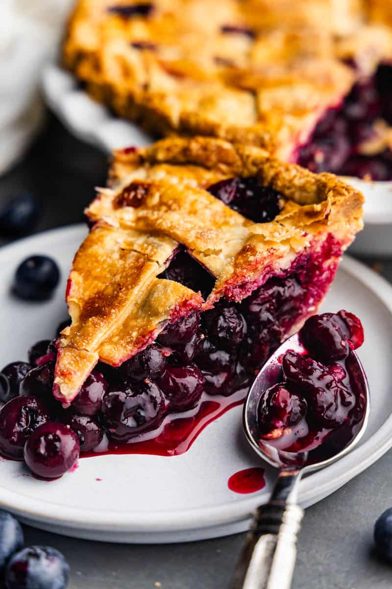 Slice of freshly baked blueberry pie on white plate.