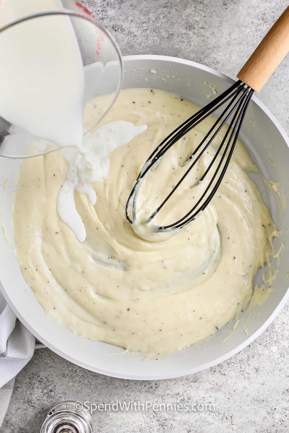 Adding milk to potatoes au gratin sauce in a skillet