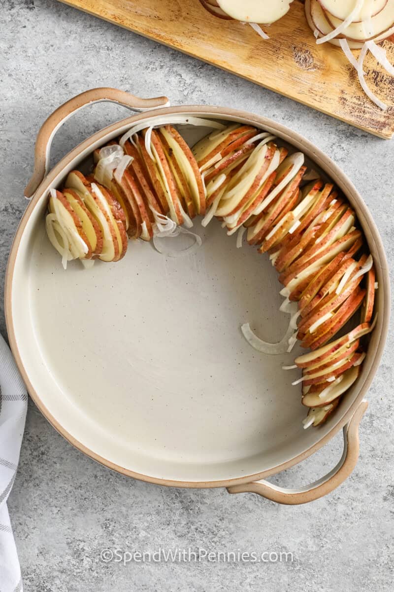 Placing sliced potatoes and onions in a dish for potatoes au gratin