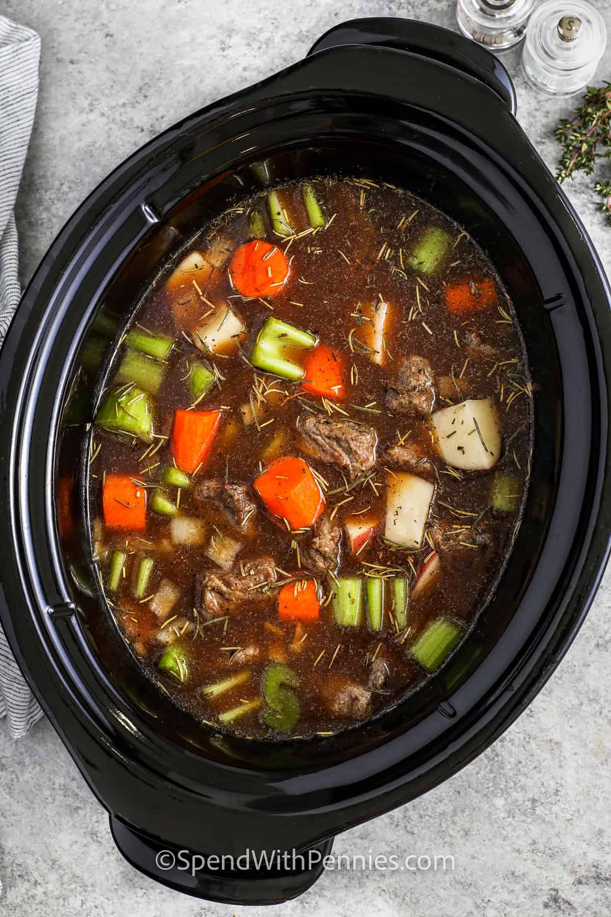 Nothing says comfort like Crockpot beef stew! Juicy beef, hearty potatoes, and flavorful veggies are slow-cooked in a rich broth for a dish that’s as satisfying as it is easy. Prep it in minutes, and let the slow cooker do the rest. Whether it’s a family dinner or meal prep for the week, this recipe always hits the spot. #spendwithpennies adding broth and seasonings to ingredients to make Crock Pot Beef Stew