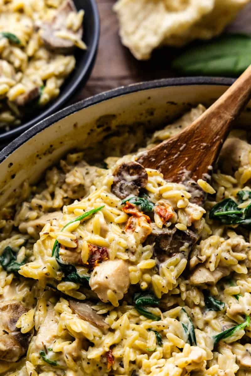 A wooden spoon scooping a helping of one pot italian pasta orzo