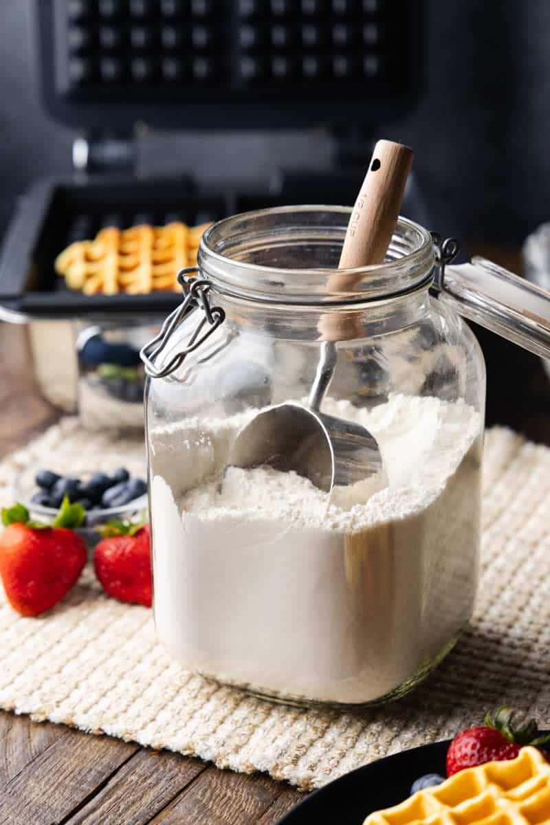 A large jar of homemade waffle mix with a scoop in it.