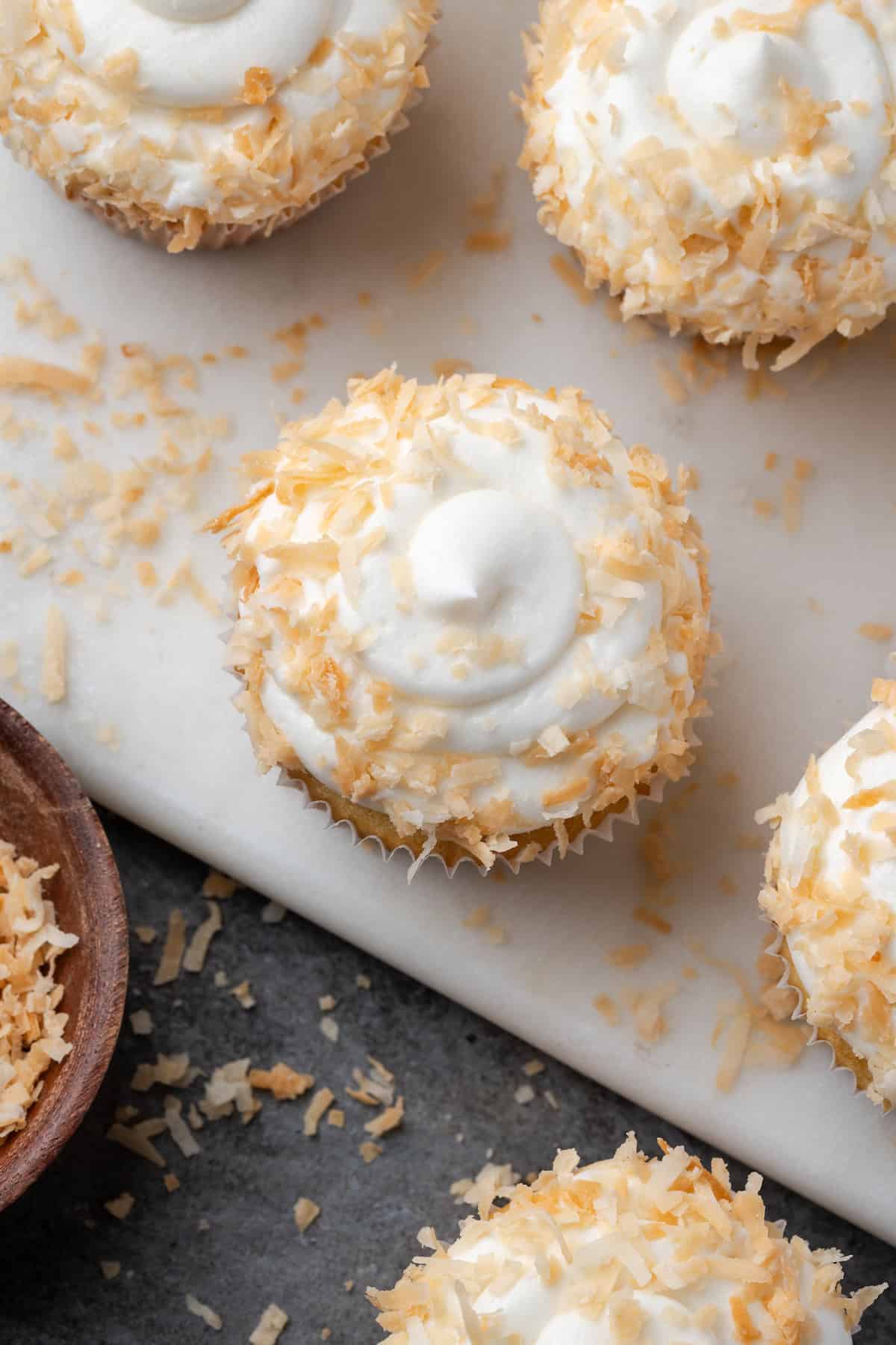 Overhead view of almond cupcakes with swirls of coconut buttercream topped with toasted coconut.