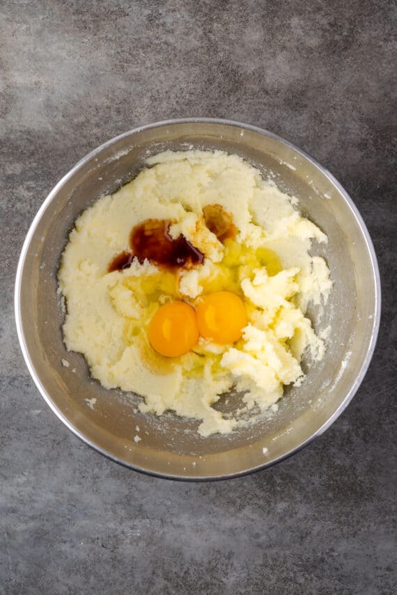 Eggs and vanilla added to creamed wet ingredients in a mixing bowl.