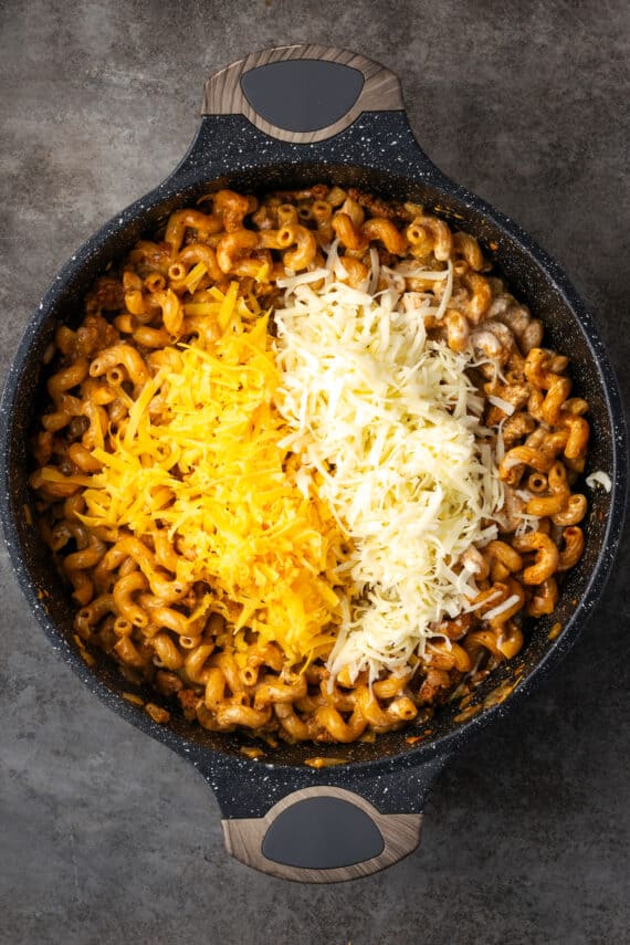 Shredded cheese added to the cheeseburger noodle mixture in a skillet.