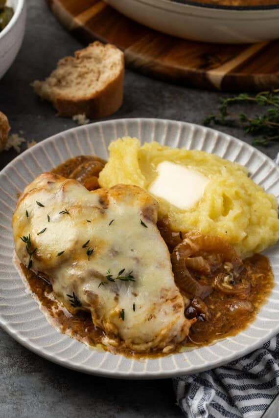 French onion chicken on a plate with a side of mashed potatoes and onion gravy.