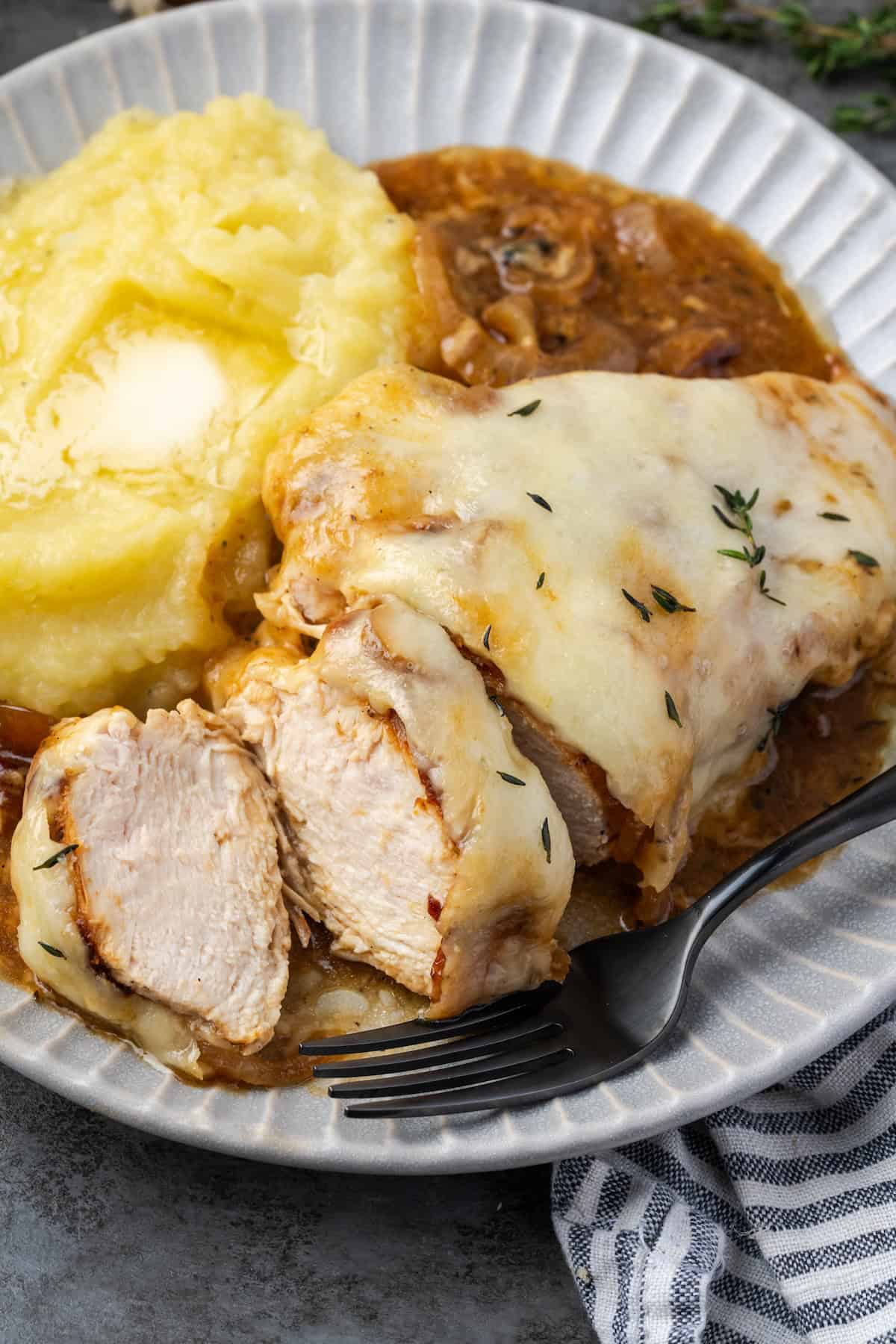 French onion chicken sliced on a plate with a side of mashed potatoes and onion gravy.