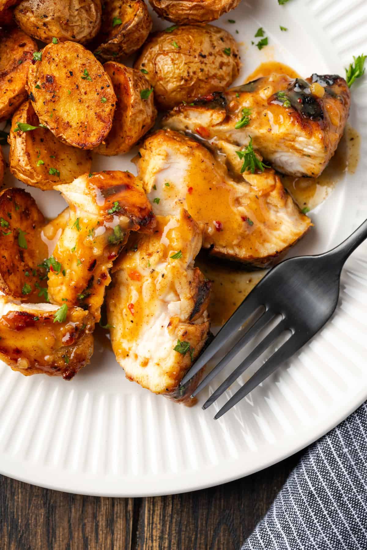 Overhead view of honey mustard chicken slices on a plate next to a fork and roasted potatoes.