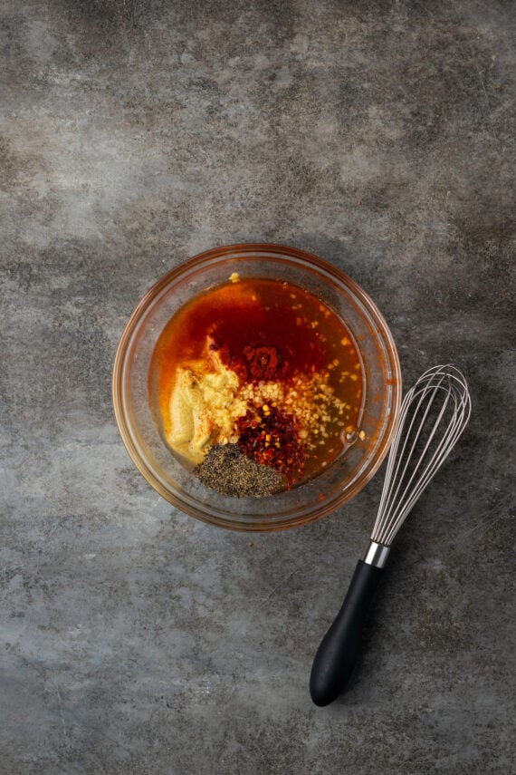 Honey mustard sauce ingredients combined in a glass bowl next to a whisk.