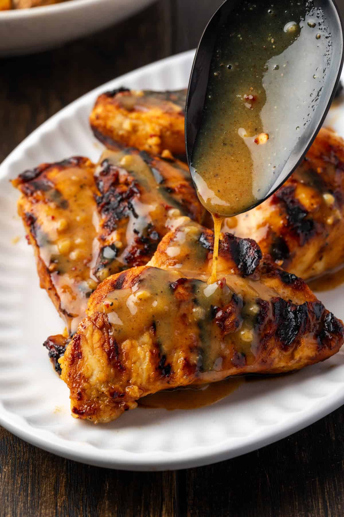 A large spoon drizzling honey mustard sauce over honey mustard chicken on a white platter.