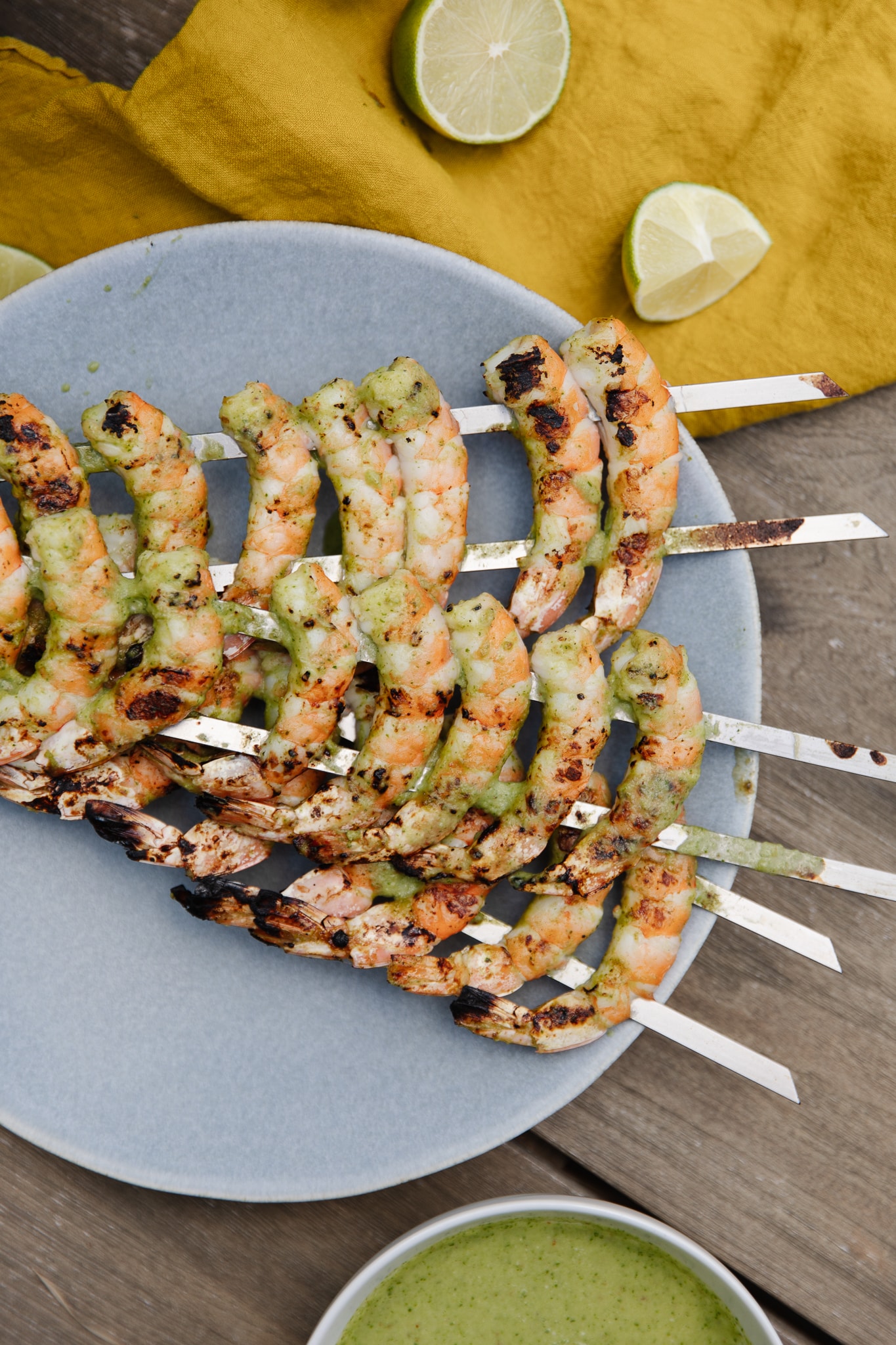 Steel skewers of grilled shrimp on a platter drizzled with a spicy green sauce