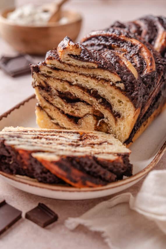 A chocolate babka on a long plate with a slice cut from the end.