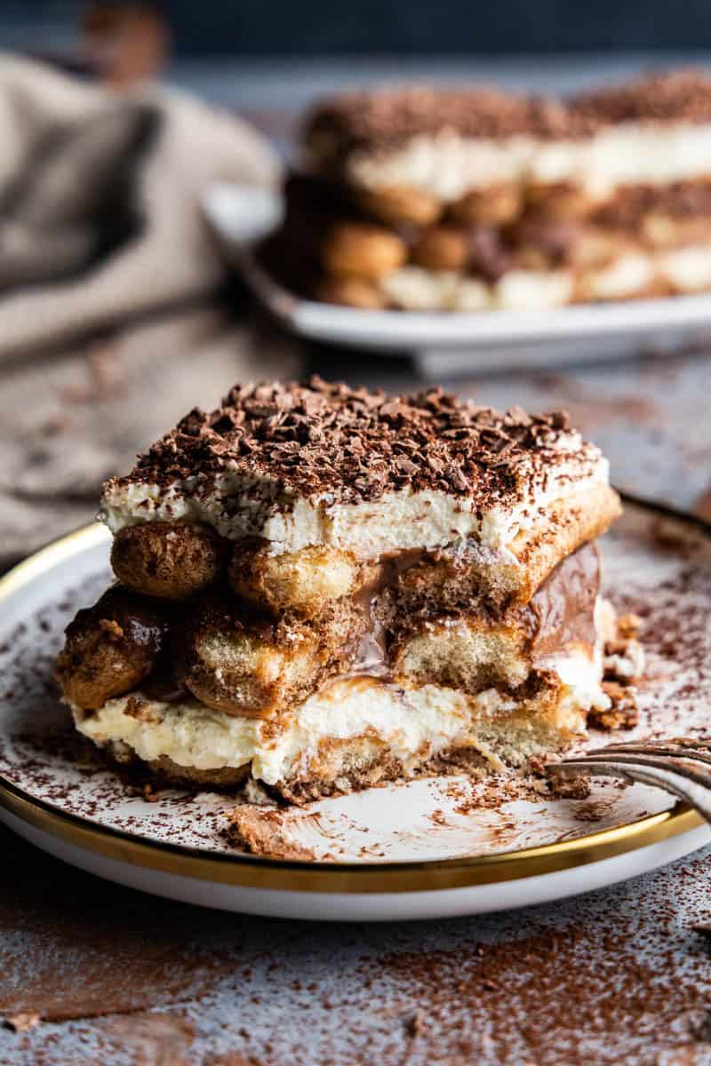 Angled shot of tiramisu slice with a bite taken out of it on a plate.