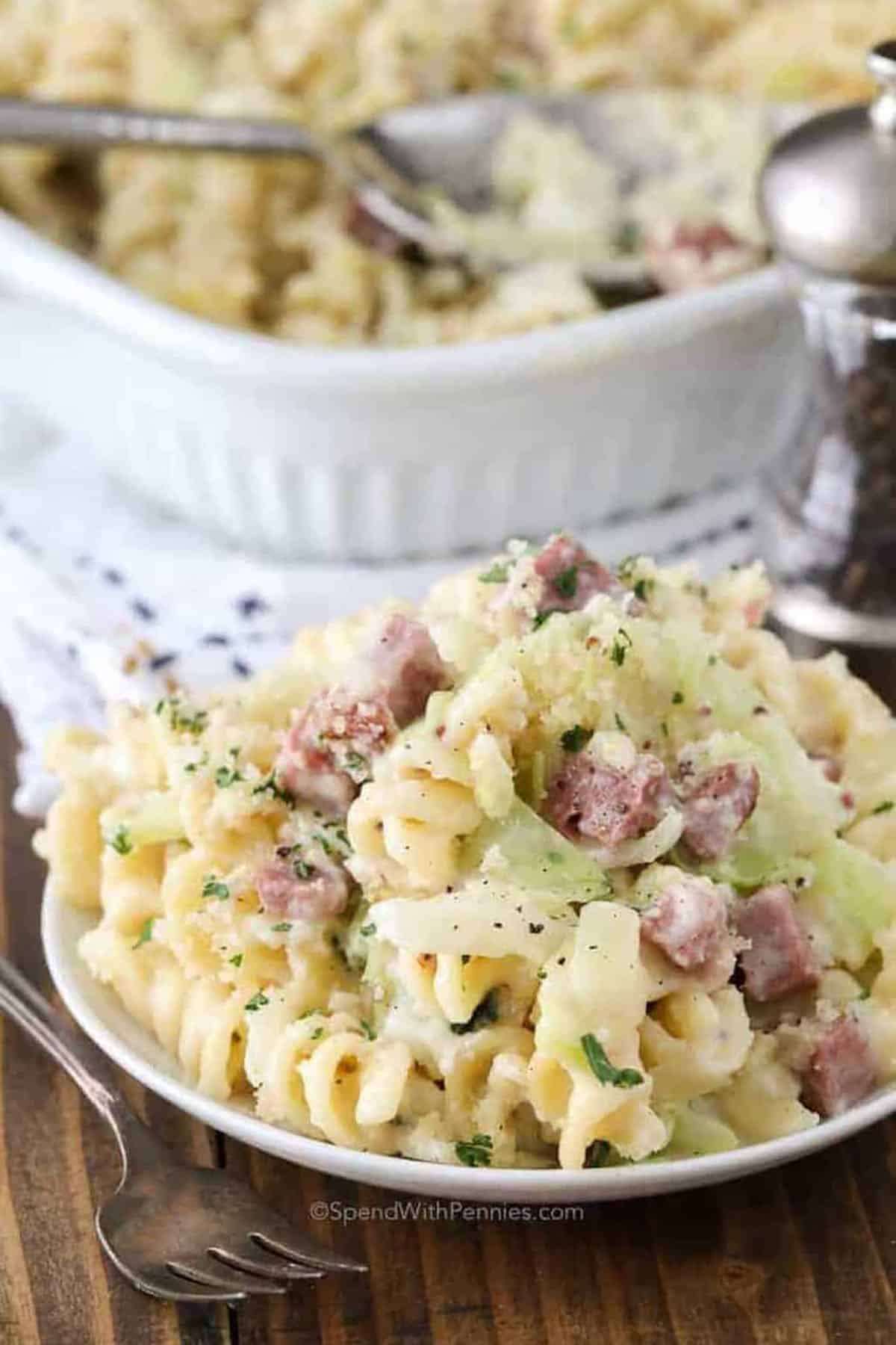 Cook this delicious, hearty Rueben nooel3 casserole for dinner and enjoy all the great flavors of the classic sandwich in one easy to serve dish. Layers of rotini past and savory corned beef meld with sauerkraut and melted Swiss cheese, while a zesty sauce ties all the flavors together. Bake until the bread crumb and parmesan topping is crispy and golden. with a crispy topping, It’s the perfect make-ahead, or make-and-take dish with crowd appeal! #spendwithpennies plated Reuben Casserole with casseroel dish full
