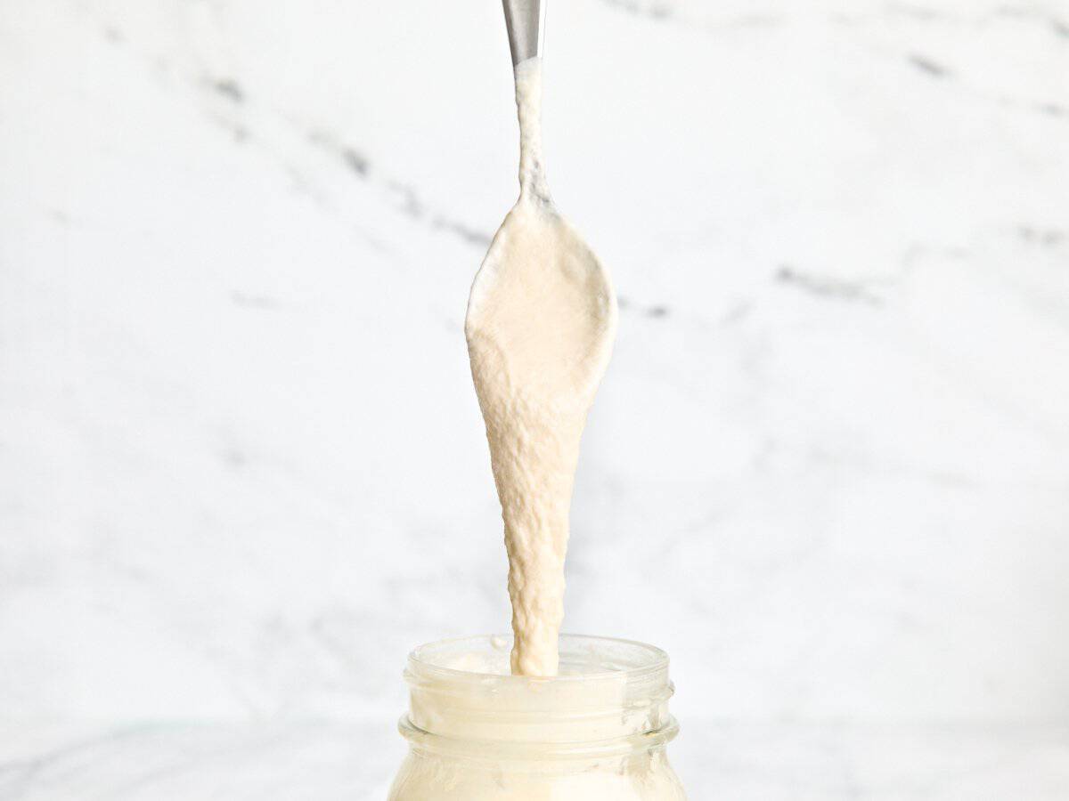 A spoon checking the consistency of a homemade sourdough starter in a mason jar.
