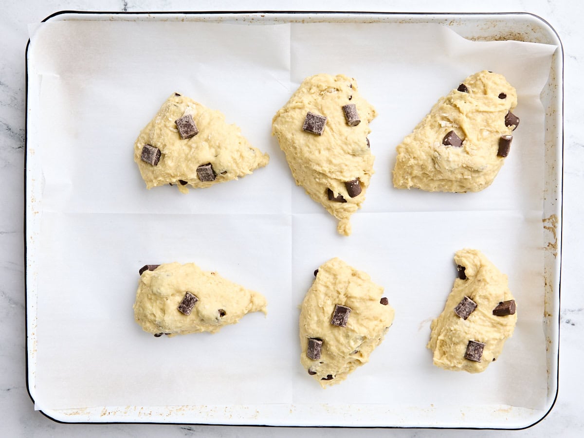 Six shaped sourdough chocolate chip scones on a parchment lined baking sheet ready to be baked.