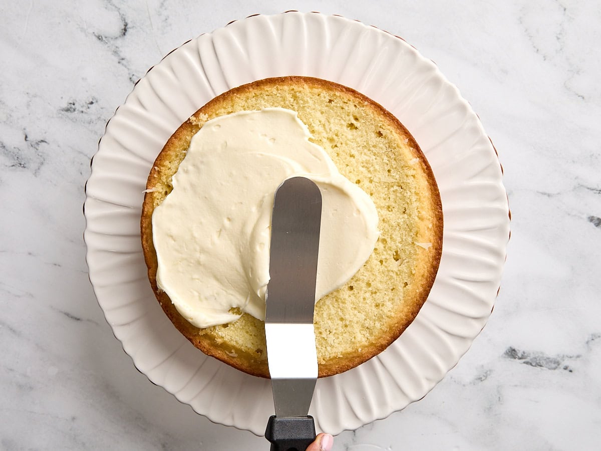 Coconut frosting being spread on an inner layer of coconut cake.