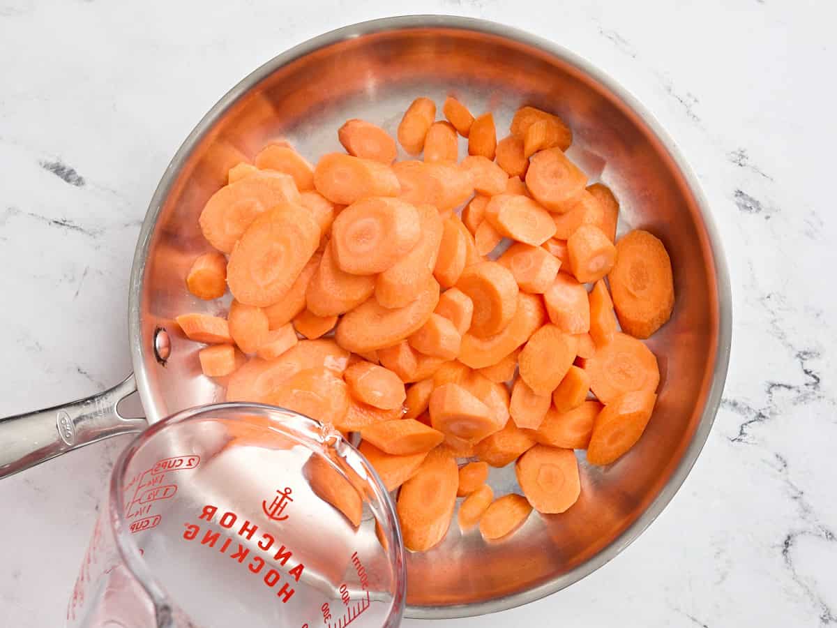 Chopped carrots in a pan with water being poured in.