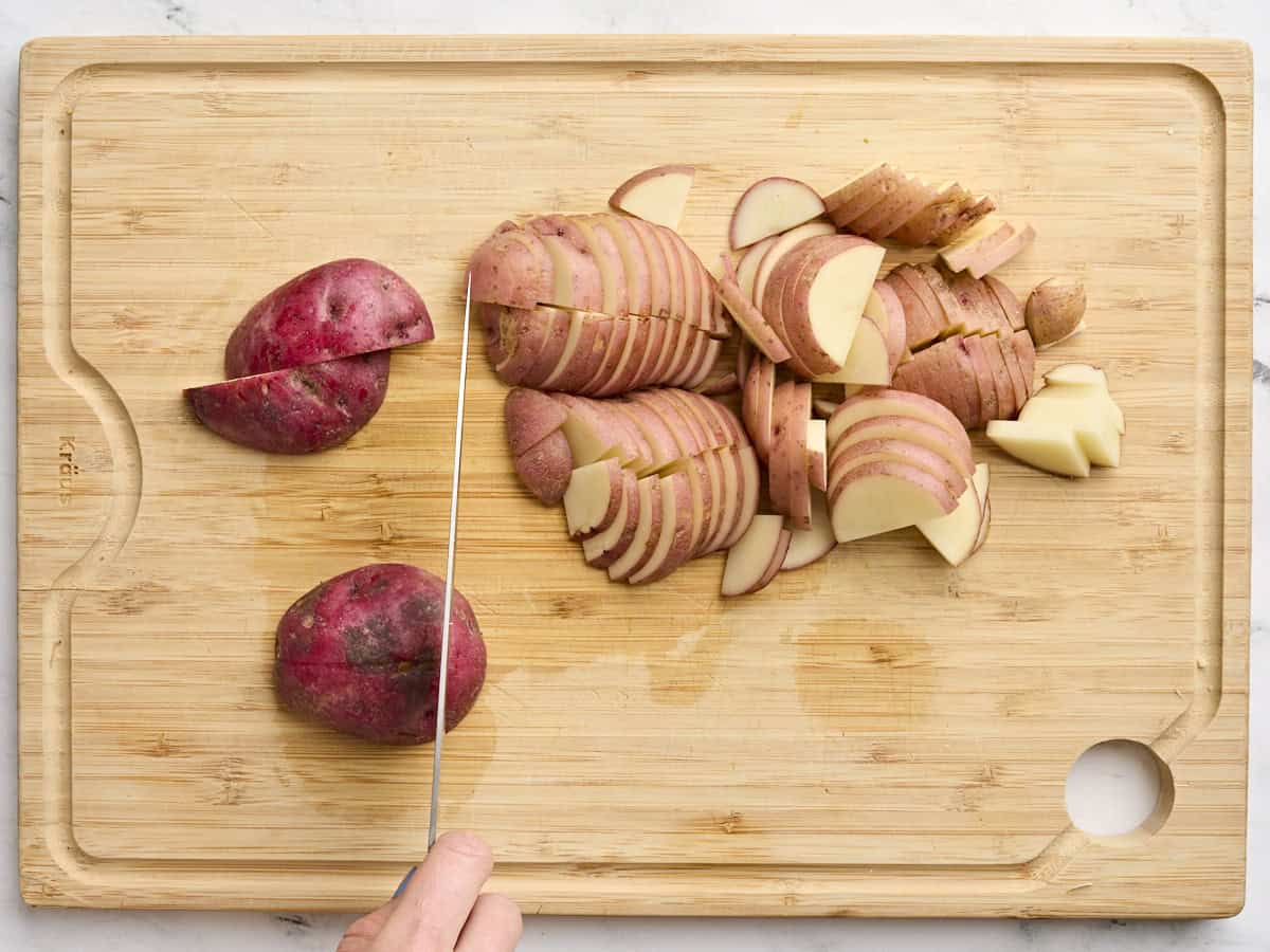 A hand slicing potatoes on a wooden cutting board.