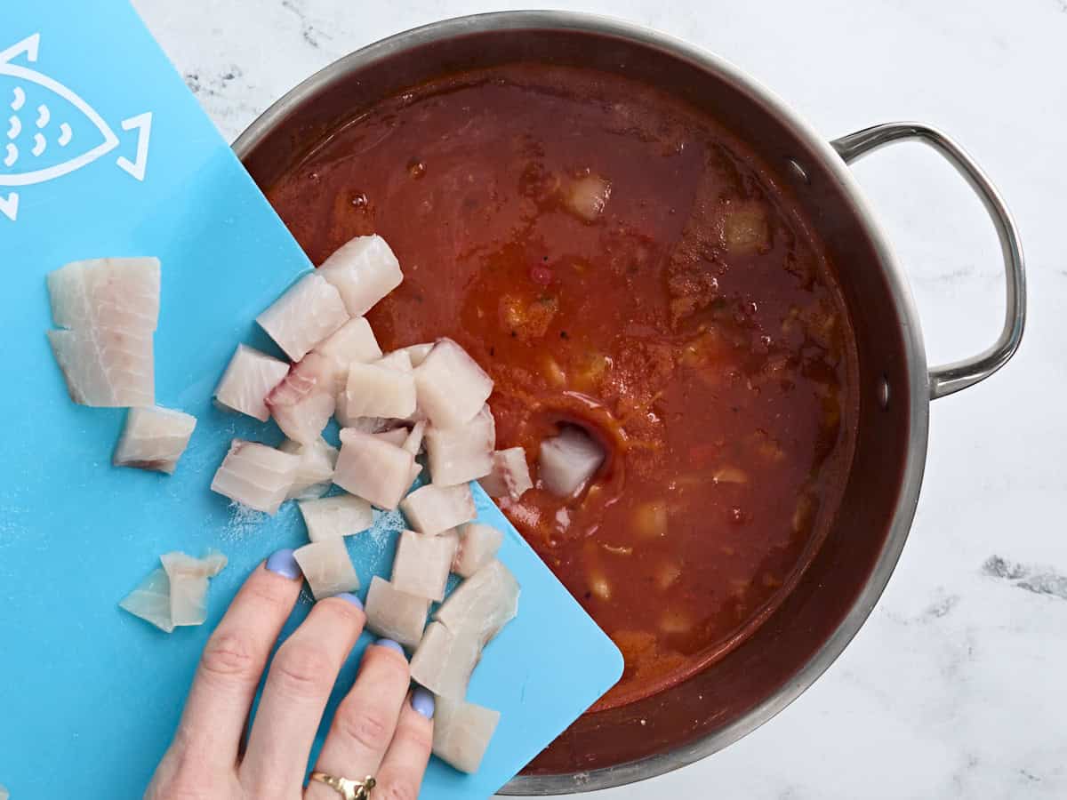 Diced tilapia being added to the tomato broth in a soup pot to make fish soup.