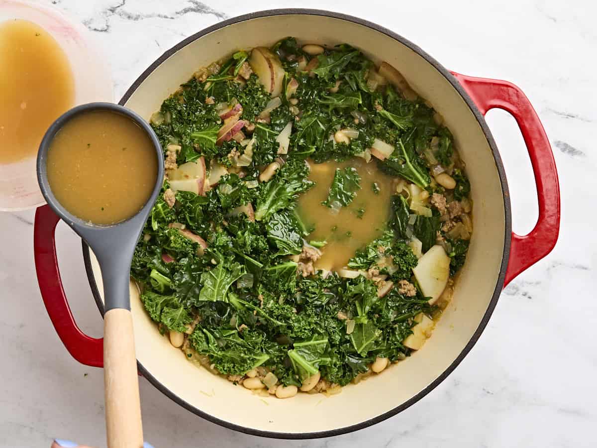 A ladle removing some broth from a pot of zuppa toscana.