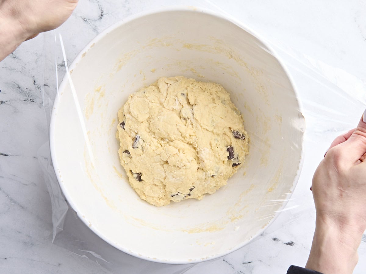 Chocolate chip sourdough scone dough in a mixing bowl, being covered with plastic wrap.