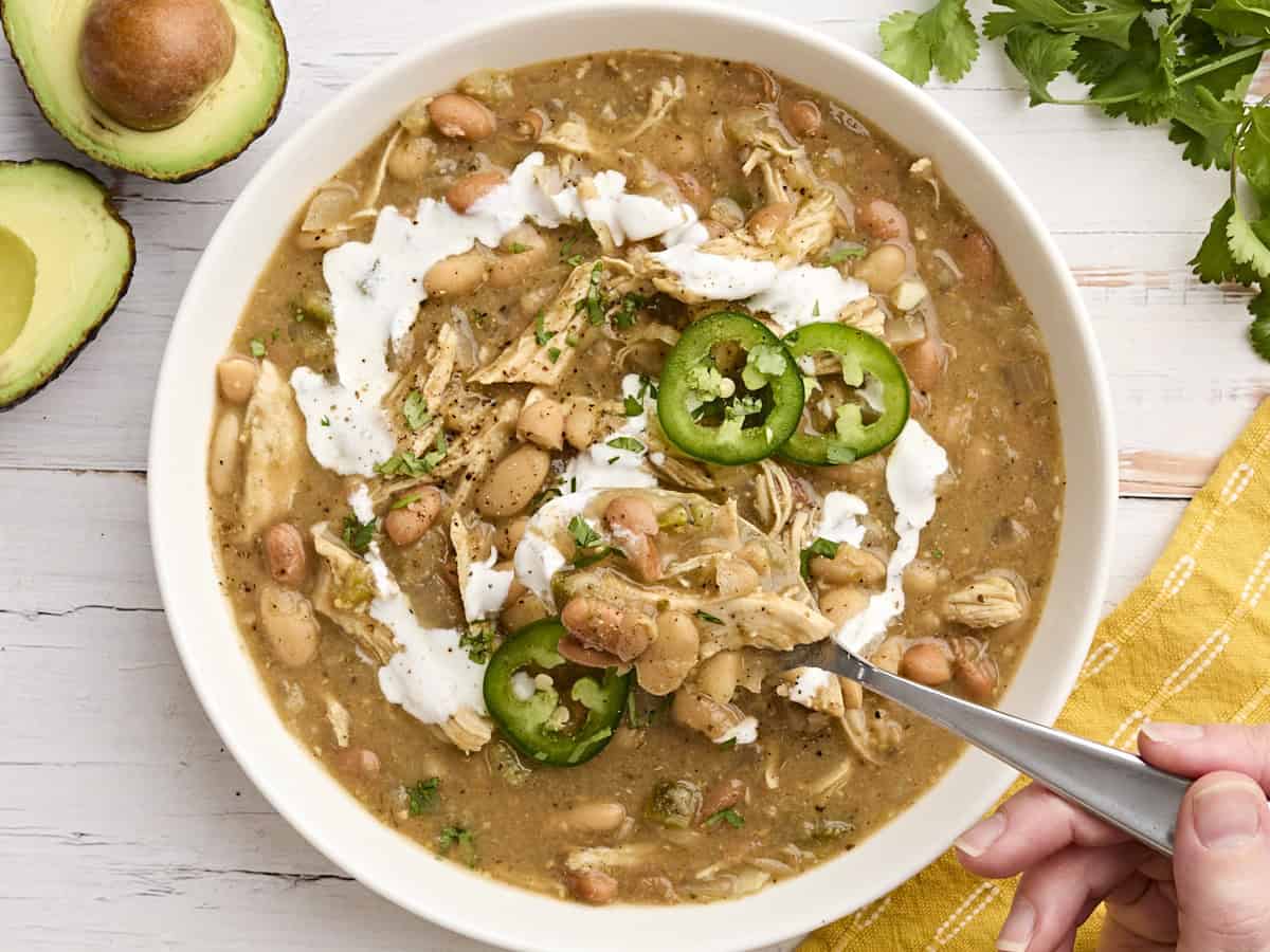 The slow cooker does all the work with this easy, flavorful, and healthy white chicken chili. This Crockpot white chicken chili in a bowl with a spoon taking some.
