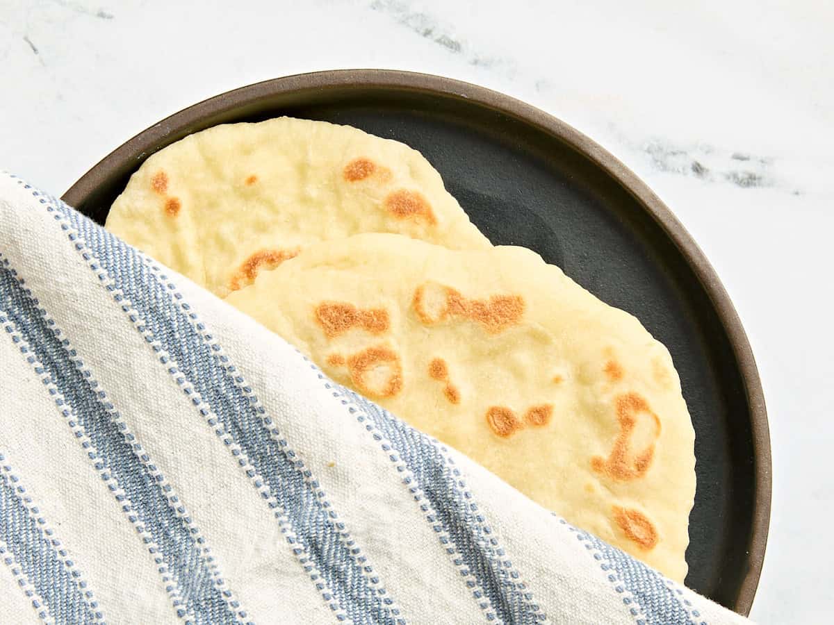 Two freshly cooked naan on a plate being covered with a kitchen towel.