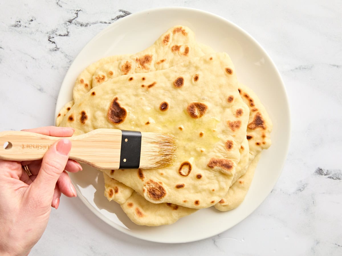 Homemade naan being brushed with melted butter.
